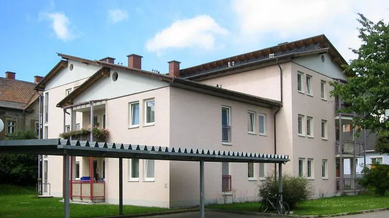 Mehrfamilienhaus mit heller Fassade, Satteldach und überdachtem Carport.
