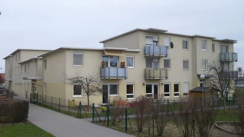 Mehrfamilienhaus mit mehreren Balkonen und einem kleinen Gartenbereich.