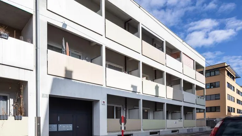 Modernes Mehrfamilienhaus mit hellen Fassaden, zahlreichen Balkonen und einer Garage im Erdgeschoss.