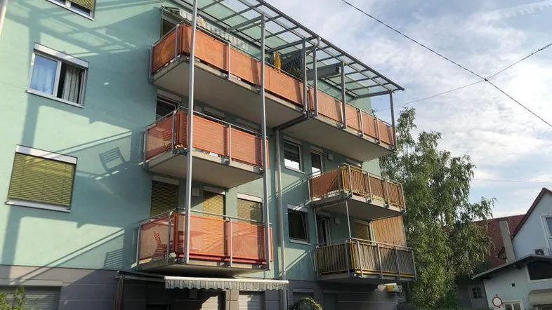 Mehrstöckiges Wohngebäude mit mintgrüner Fassade und mehreren Balkonen mit orangefarbenen Geländern.