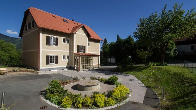 Attraktives Mehrfamilienhaus mit rotem Ziegeldach, gepflegter Auffahrt und grüner Umgebung.