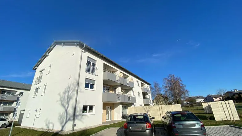 Modernes Neubau-Wohngebäude mit zeitgenössischer Architektur, Balkonen und Außenparkplätzen unter blauem Himmel.
