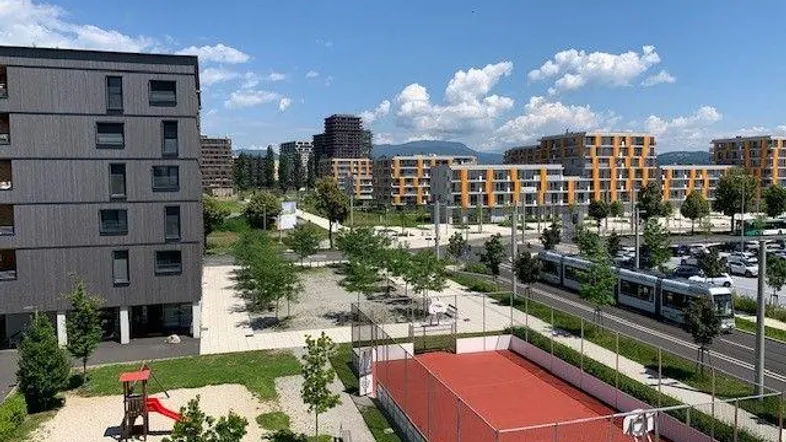 Weitläufige Außenansicht einer modernen Wohnsiedlung mit Spielplatz, Sportplatz und Straßenbahnhaltestelle.