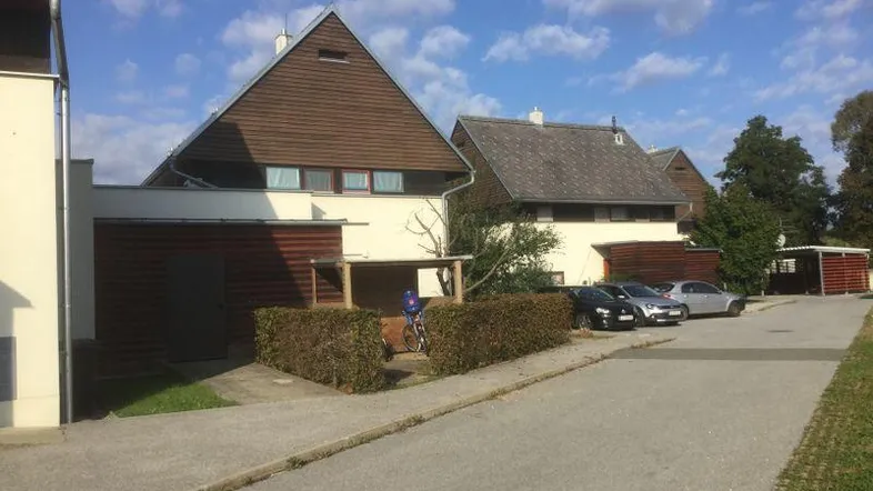 Reihenhäuser mit markanten Holzgiebeldächern und hellen Fassaden entlang einer Wohnstraße mit Parkplätzen.