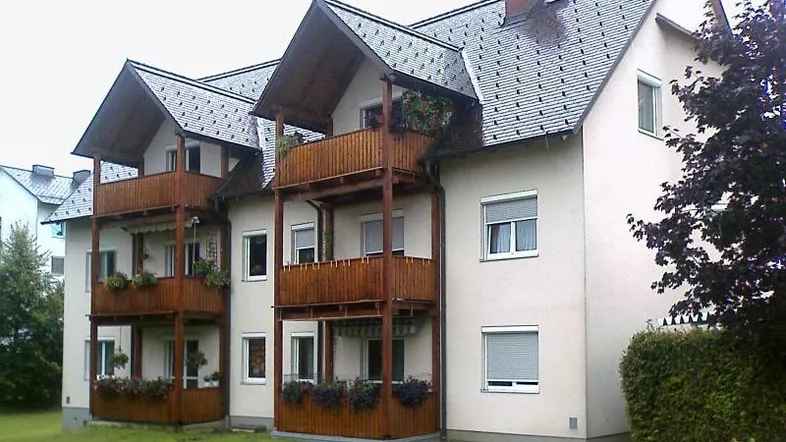 Mehrfamilienhaus mit mehreren Balkonen und Satteldach in grüner Umgebung, gut gepflegt.