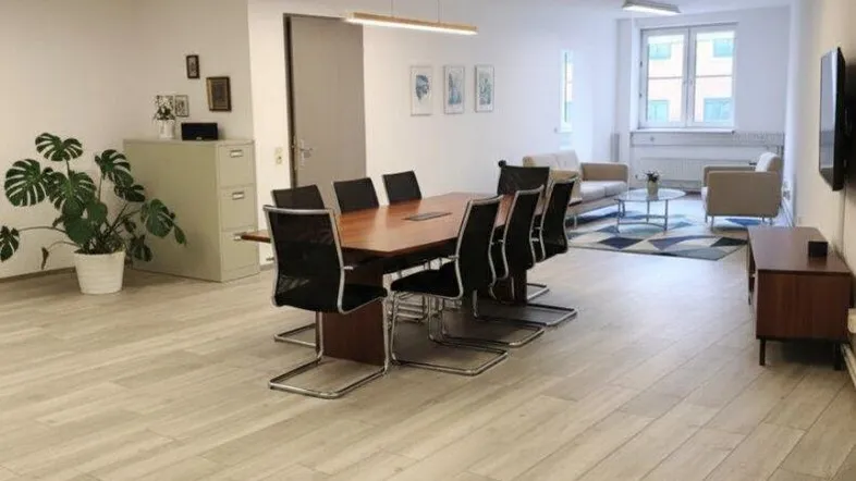 Geräumiger Büroraum mit Konferenztisch, Sitzbereich und großen Fenstern für natürliches Licht.