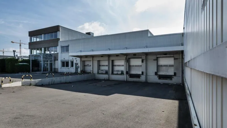 Industrielles Gebäude mit mehreren Laderampen und einem angrenzenden Bürokomplex unter blauem Himmel.