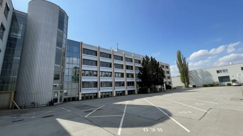 Modernes Bürogebäude mit Glasfassade und großem Parkplatz unter blauem Himmel.