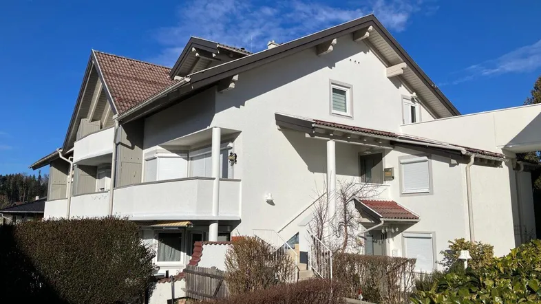 Mehrfamilienhaus mit mehreren Balkonen und gepflegter Außenanlage unter blauem Himmel.