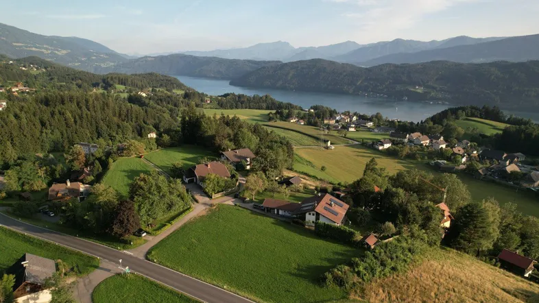 Panoramablick auf eine malerische Seenlandschaft mit umliegenden Bergen und vereinzelten Häusern.