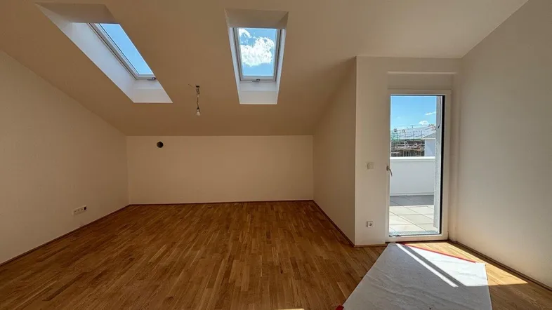Heller Wohnraum im Dachgeschoss mit Holzboden, Dachfenstern und Zugang zur Terrasse.