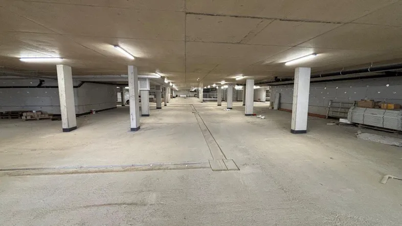 Unfertige Tiefgarage mit Betonboden, Säulen und Beleuchtung, bereit für den Ausbau.