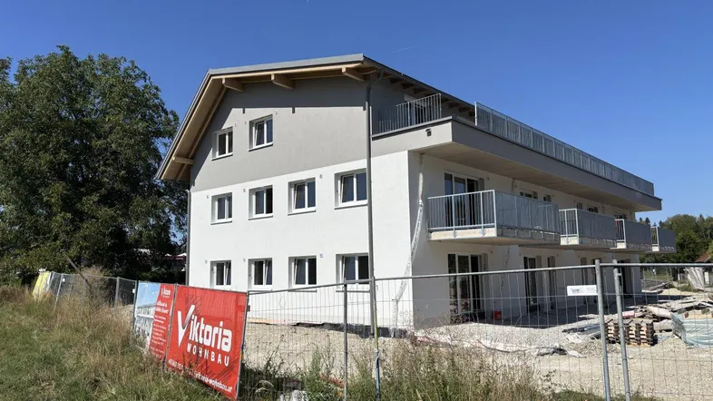 Neubau eines Mehrfamilienhauses im Rohbauzustand mit Balkonen und Baustellenschild bei Sonnenschein.