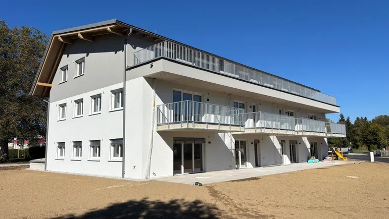 Modernes Mehrfamilienhaus mit Balkonen und Dachterrasse in sonniger Lage, umgeben von Grünflächen.