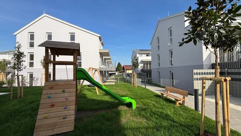 Neubauwohnungen mit modernem Spielplatz, Rasenfläche und Sitzbank im Außenbereich.