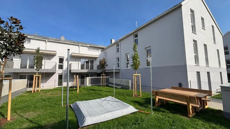 Neubauwohnungen mit Gemeinschaftsgarten und Sitzbereich im Freien unter blauem Himmel.