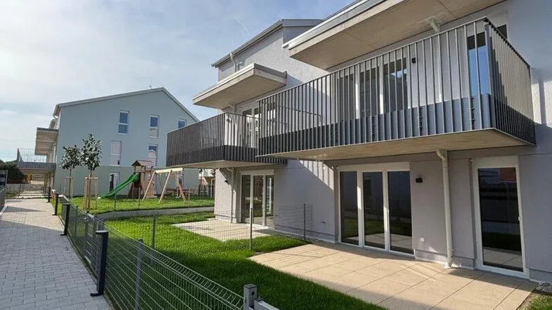 Moderne Wohnanlage mit Balkonen, Terrassen und kleinen Gärten, umgeben von einem gepflegten Gehweg.