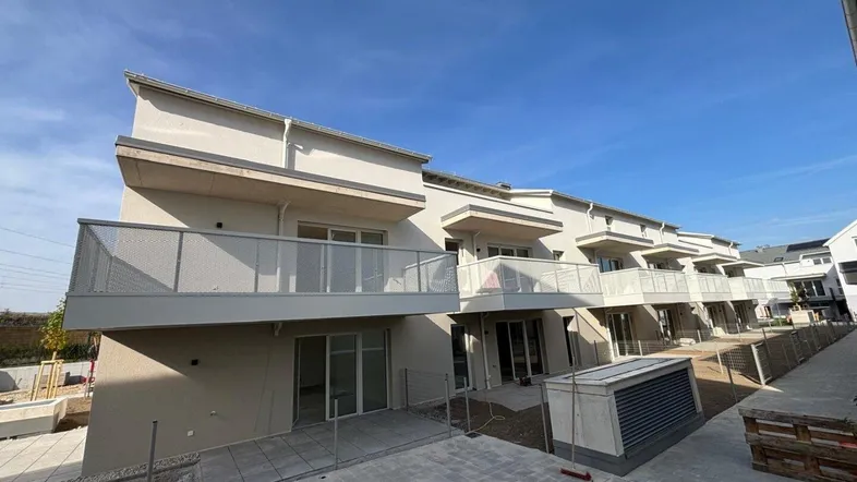 Moderne Neubauwohnungen mit Balkonen und Terrassen in einer zeitgenössischen Wohnanlage unter blauem Himmel.