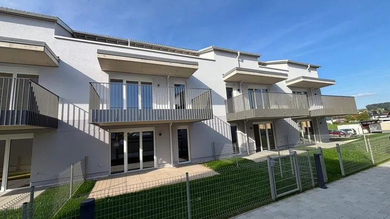 Moderne Wohnanlage mit mehreren Balkonen und Terrassen im Erdgeschoss, umgeben von Grünflächen.