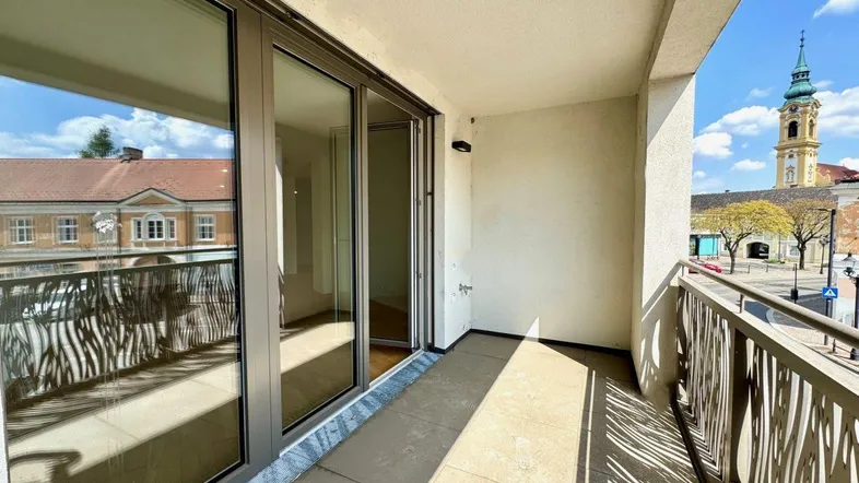 Heller Balkon mit Blick auf den Stadtplatz und einen Kirchturm, ausgestattet mit modernen Glas-Schiebetüren.