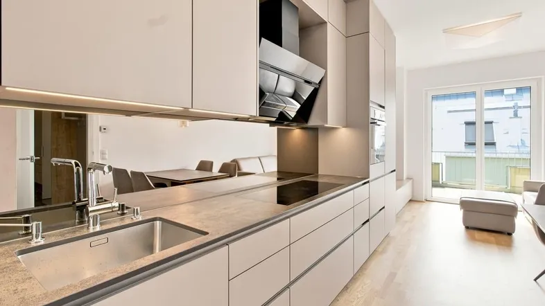 Moderne Einbauküche mit hellen Fronten, integrierten Geräten und Blick auf den Wohnbereich.