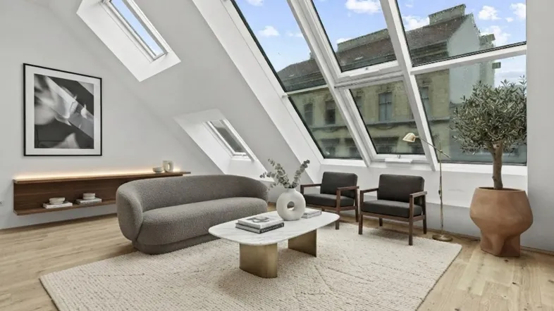 Helles Dachgeschoss-Wohnzimmer mit großen Fenstern, Holzboden und moderner Einrichtung.