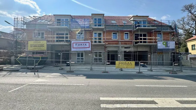 Neubauprojekt im Bau mit Gerüst und Verkaufsbannern an der Fassade, von der Straße aus gesehen.