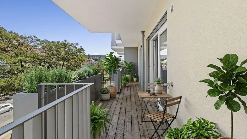 Heller Balkon mit Holzboden, Pflanzen und kleinem Tisch, ideal zum Entspannen im Freien.