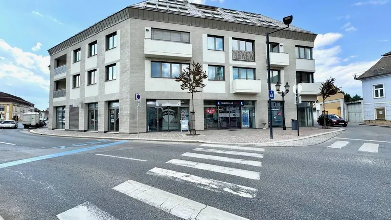 Modernes Eckgebäude mit Geschäften im Erdgeschoss und Wohnungen darüber, an einer belebten Kreuzung gelegen.