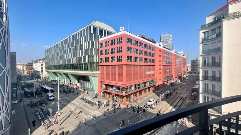 Stadtansicht mit modernen Gebäuden, belebten Straßen und klarem Himmel von einem Balkon aus.