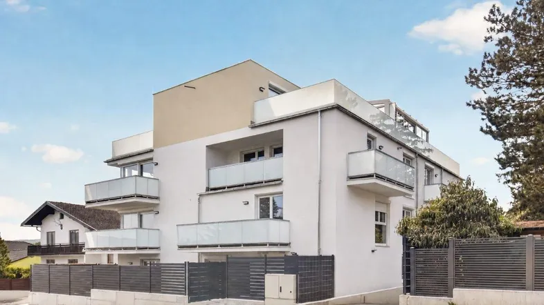 Modernes Mehrfamilienhaus mit Balkonen und gepflegter Außenanlage unter blauem Himmel.
