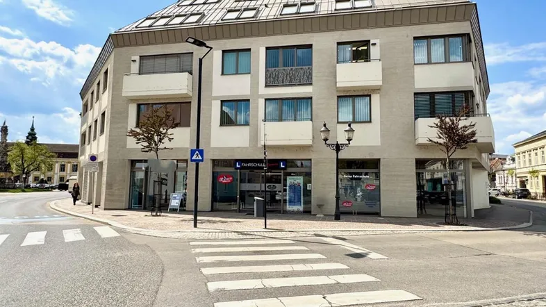 Modernes Eckgebäude mit Geschäften im Erdgeschoss und Wohnungen darüber, an einer belebten Straßenkreuzung gelegen.