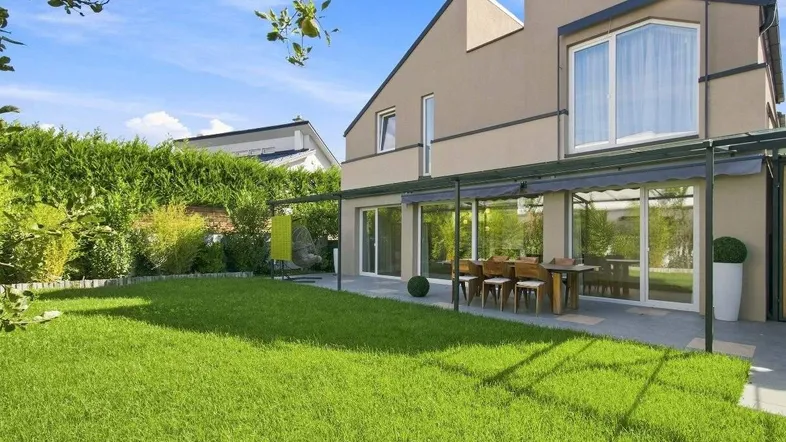Modernes Haus mit großem, gepflegtem Garten und möblierter Terrasse für Mahlzeiten im Freien.