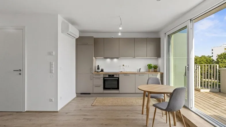 Moderne Küche mit integrierten Geräten, kleinem Essbereich und Zugang zu einer sonnigen Terrasse.
