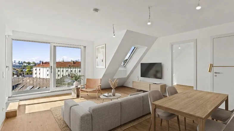 Heller Wohn- und Essbereich mit Holzboden, Dachschrägen und Zugang zum Balkon.