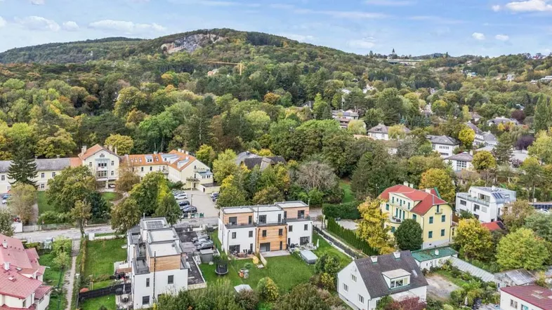 Luftaufnahme einer Wohnsiedlung mit modernen Reihenhäusern und viel Grün in hügeliger Umgebung.