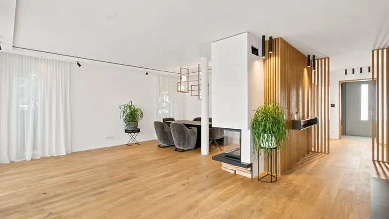 Moderner offener Wohn- und Essbereich mit Holzboden, Kamin und dekorativen Holzlamellen.