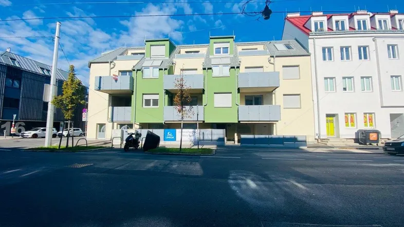 Modernes Mehrfamilienhaus mit grünen Balkonen und heller Fassade an einer Stadtstraße.