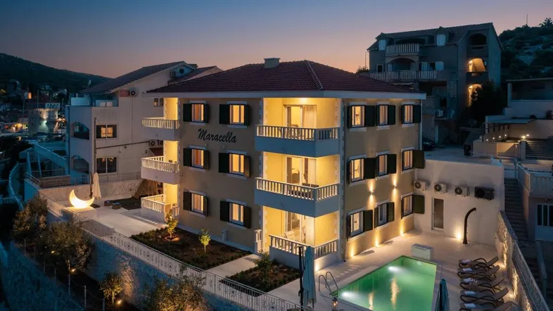 Modernes Apartmentgebäude bei Nacht mit beleuchtetem Poolbereich und Meerblick.