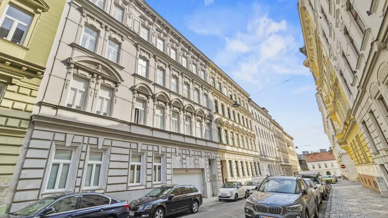 Historisches Gebäude in einer städtischen Straße mit geparkten Autos und klassischer Architektur.