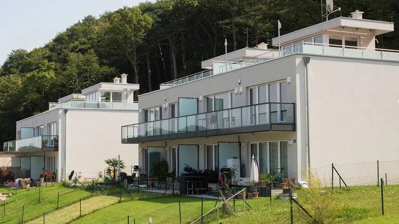 Moderne Wohngebäude mit Balkonen und Terrassen, eingebettet in eine grüne Hügellandschaft mit Bäumen.