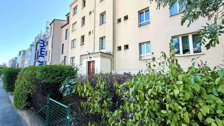 Fassade eines Mehrfamilienhauses mit hellen Wänden und grünen Büschen entlang des Gehwegs.