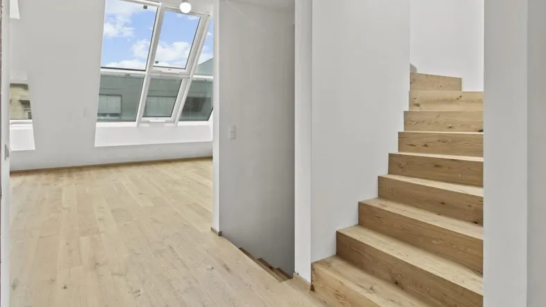 Heller Raum mit Holztreppe und großen Dachfenstern, die viel Tageslicht hereinlassen.