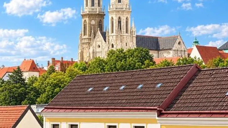 Blick auf eine belebte Straße mit Geschäften und einer historischen Kirche im Hintergrund unter blauem Himmel.