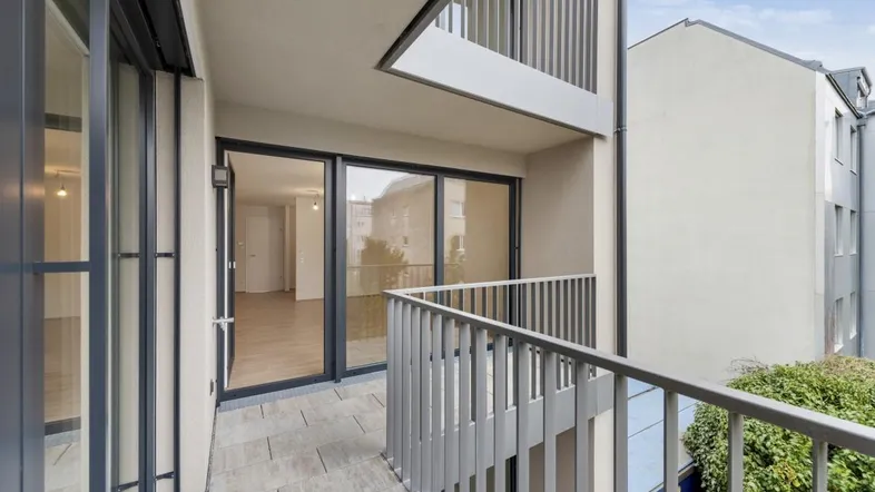 Moderner Balkon mit Fliesenboden und Blick auf den Innenhof eines Wohngebäudes.