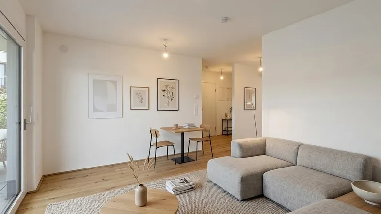 Helles Wohn- und Esszimmer mit modernem Sofa, Holzboden und Zugang zum Balkon.