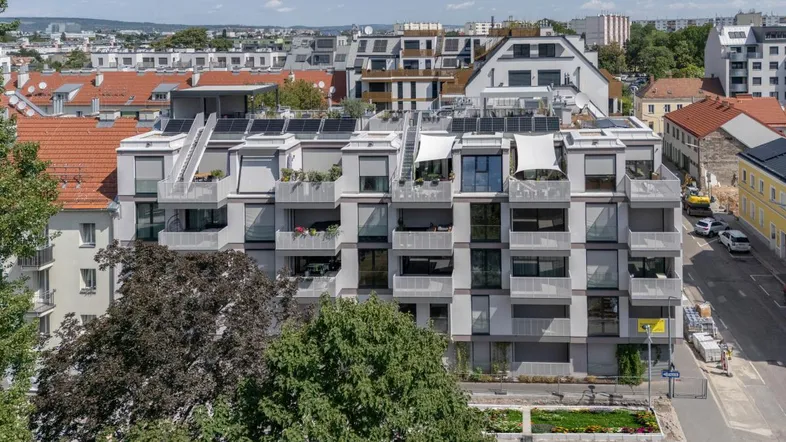 Modernes Mehrfamilienhaus mit Balkonen, Dachterrassen und Solarpaneelen auf dem Dach.