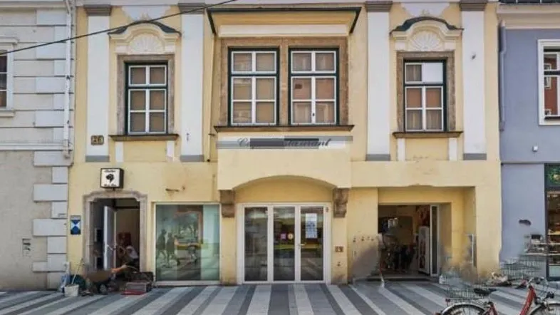Historisches Gebäude mit gelber Fassade und Geschäften im Erdgeschoss an einer belebten Straße.