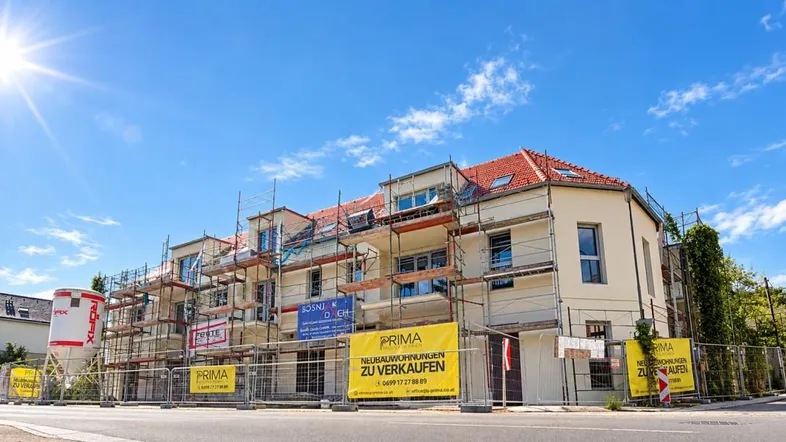 Neubauwohnungen im Bau mit Gerüst und 'Zu verkaufen'-Schildern unter strahlend blauem Himmel.