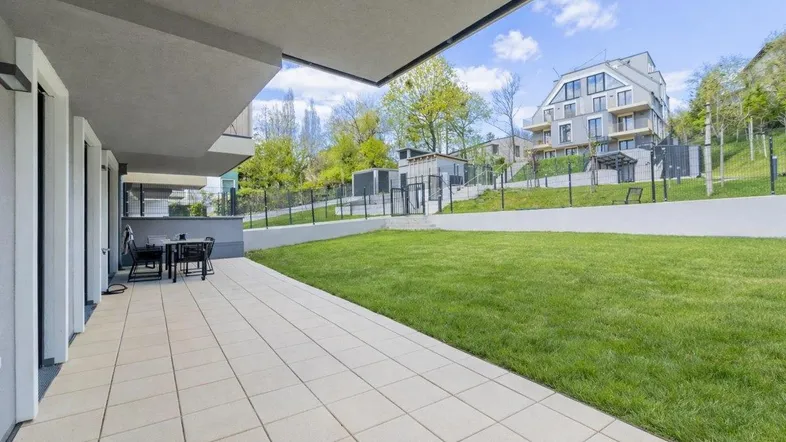 Großzügige Terrasse mit Fliesenboden und Gartenmöbeln, angrenzend an eine gepflegte Rasenfläche.